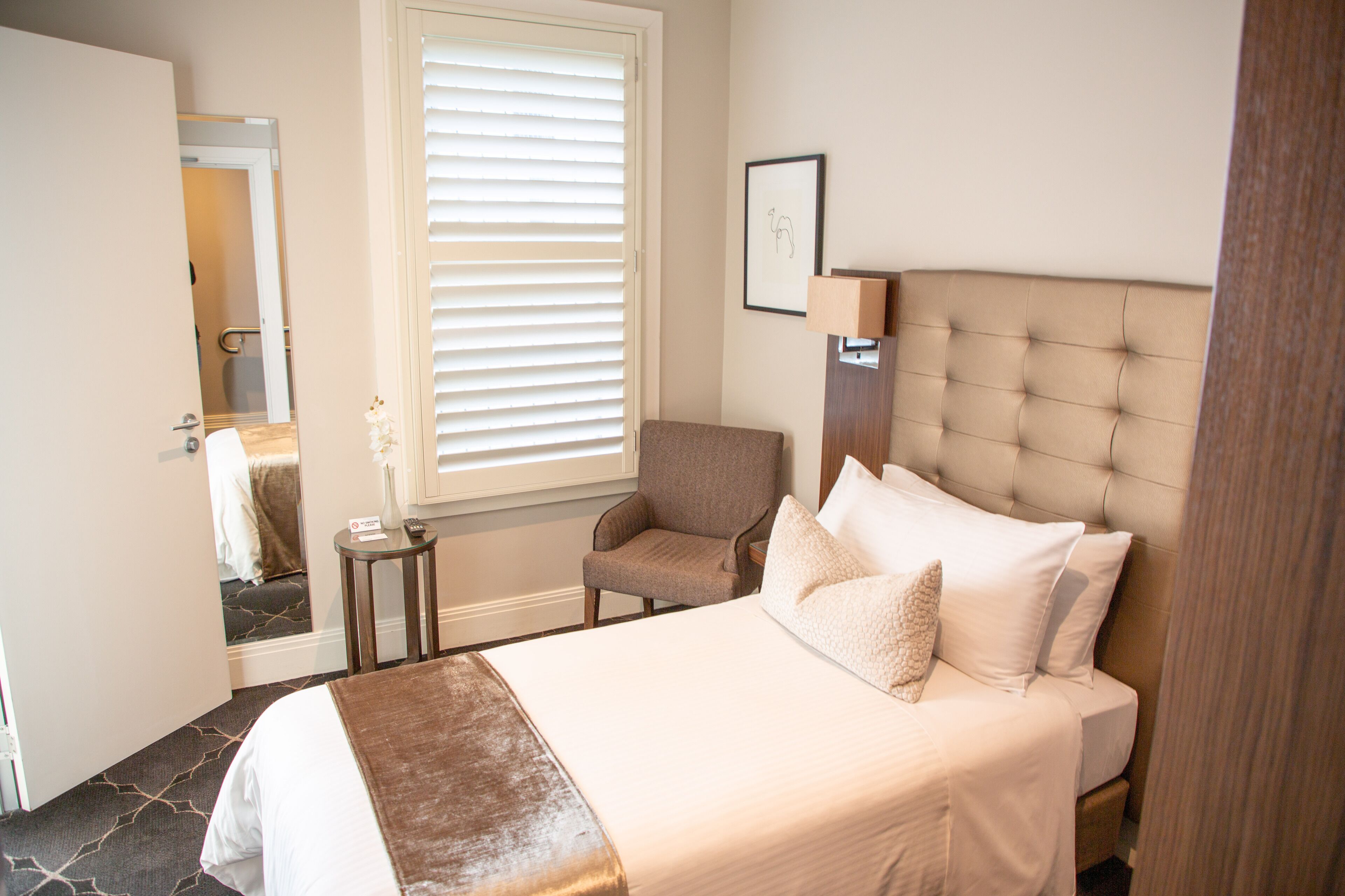 Une chambre d’hôtel avec un grand lit, une chaise, une table de chevet et une fenêtre avec des stores.