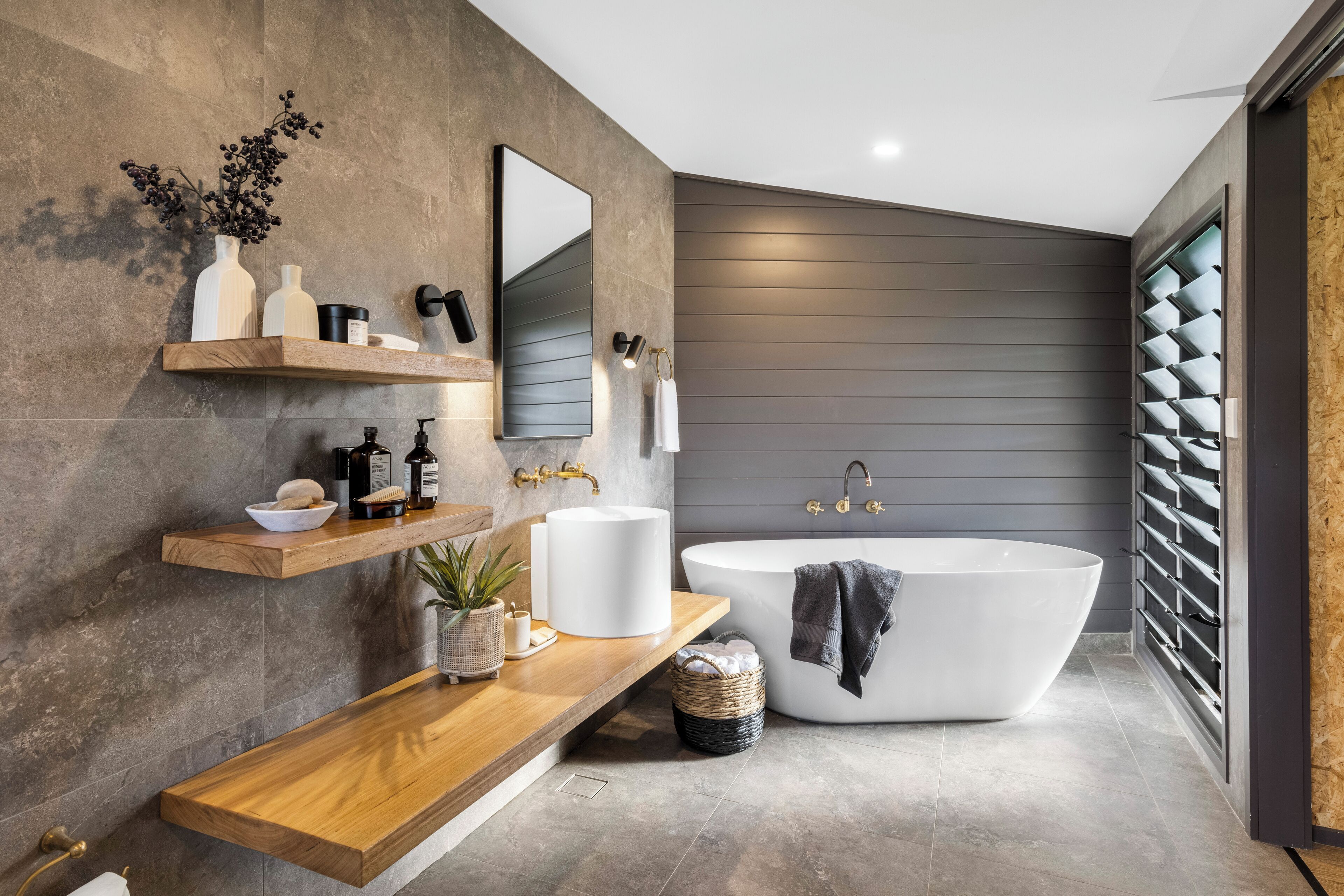 Ein modernes Badezimmer mit freistehender Badewanne, Holzregalen und einem großen Spiegel.