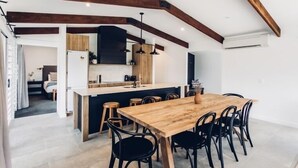 Eine moderne Küche mit einer zentralen Kochinsel, Holzbalken und schwarzen Stühlen um einen Holztisch.