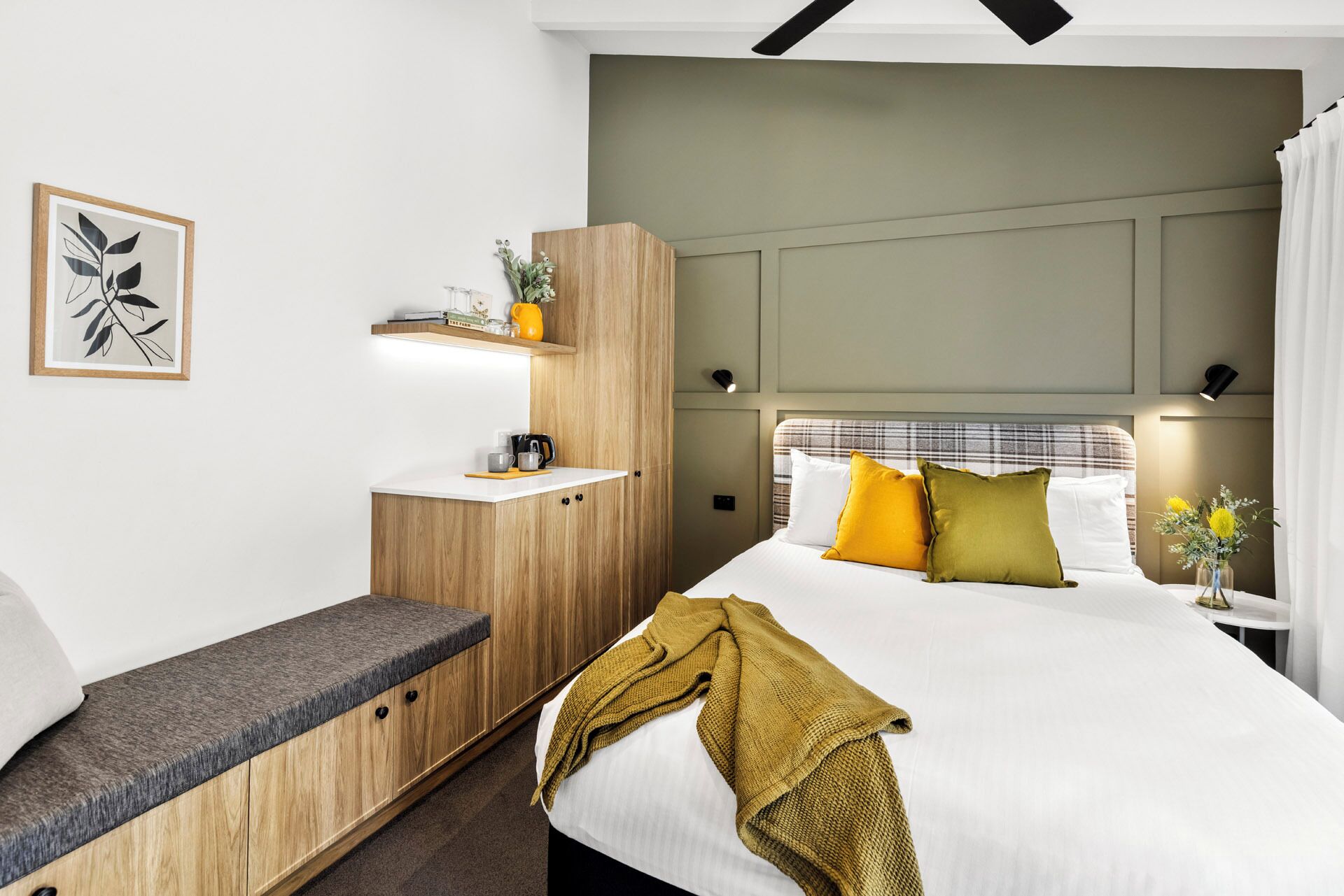 A modern hotel room with a bed, bedside table, and a small wooden cabinet with a mirror.