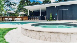 Ein moderner Poolbereich im Freien mit einer Steinterrasse, einer überdachten Terrasse und Sitzgelegenheiten.