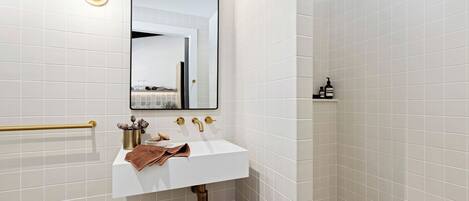 A modern bathroom with a white sink, gold fixtures, and a large mirror.