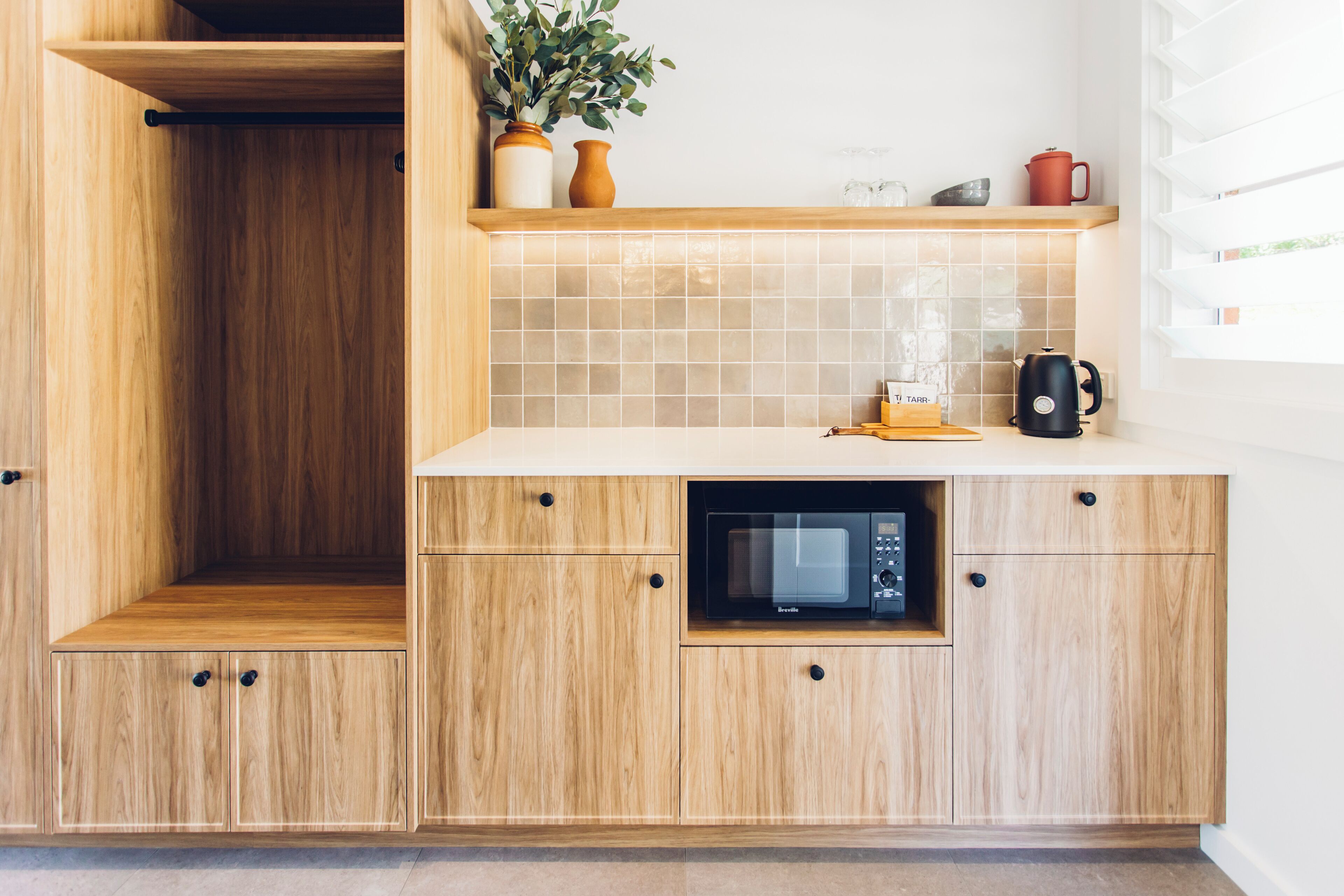 A kitchen with wooden cabinets, a microwave, and a shelf with a plant and kitchenware.
