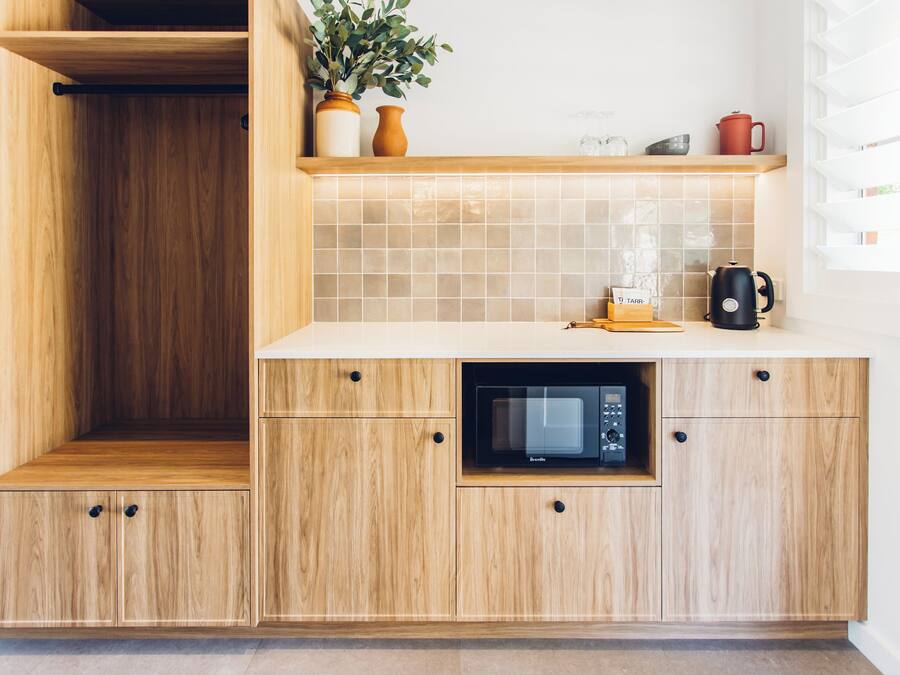 A kitchen with wooden cabinets, a microwave, and a shelf with a plant and kitchenware.