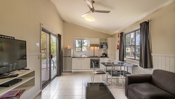 A modern living room with a flat-screen TV, a sofa, and a dining area with a table and chairs.