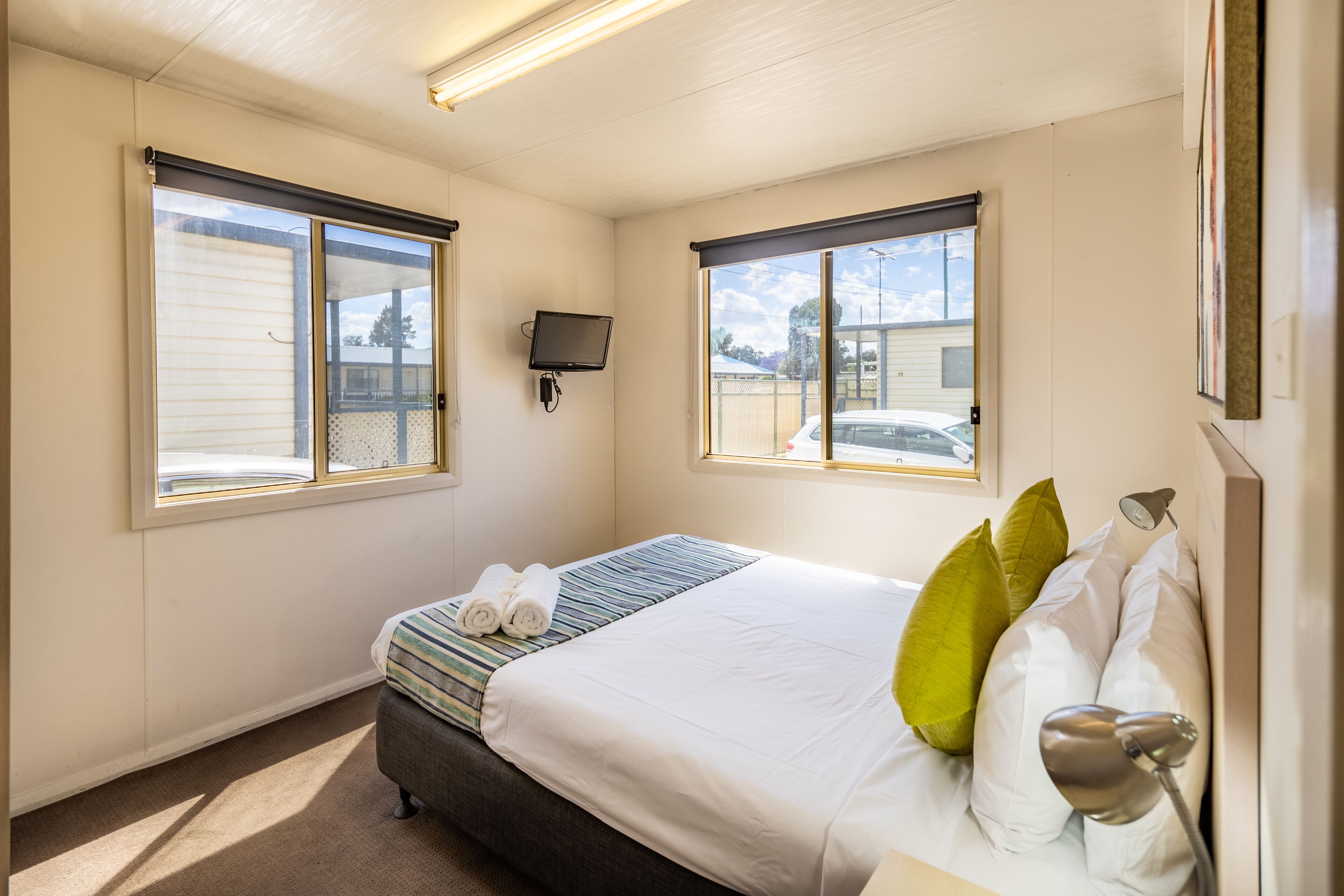 Una habitación de hotel con una cama, un televisor montado en la pared y dos ventanas.