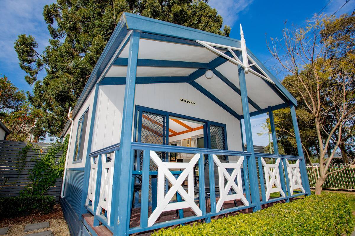 Una pequeña casa azul y blanca con techo en forma de estrella, rodeada de follaje y árboles.
