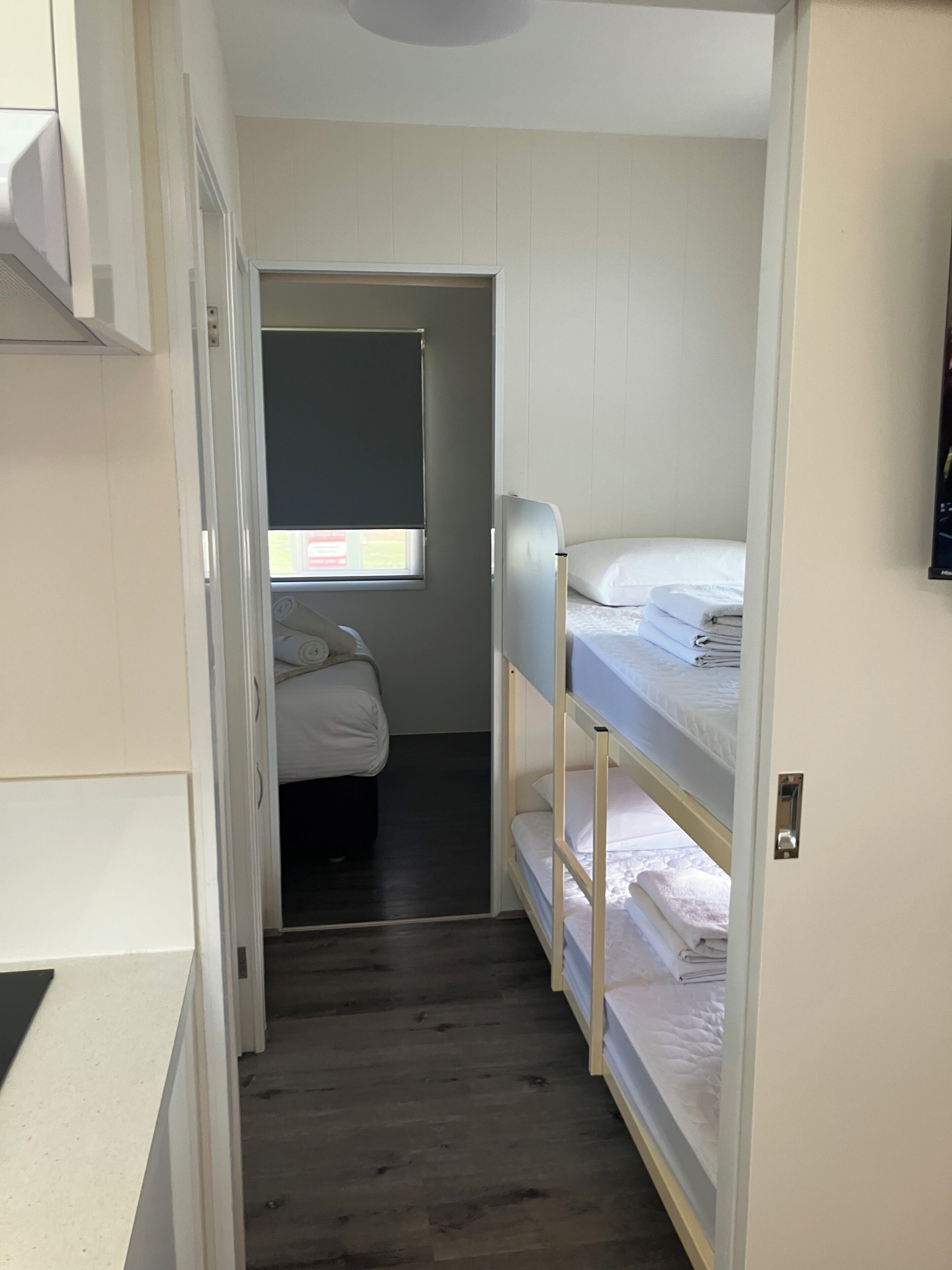 A narrow room with a bunk bed, a small window, and a door leading to another room.