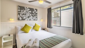 A neatly made bed with two pillows, a striped area rug, and two rolled towels on the floor.