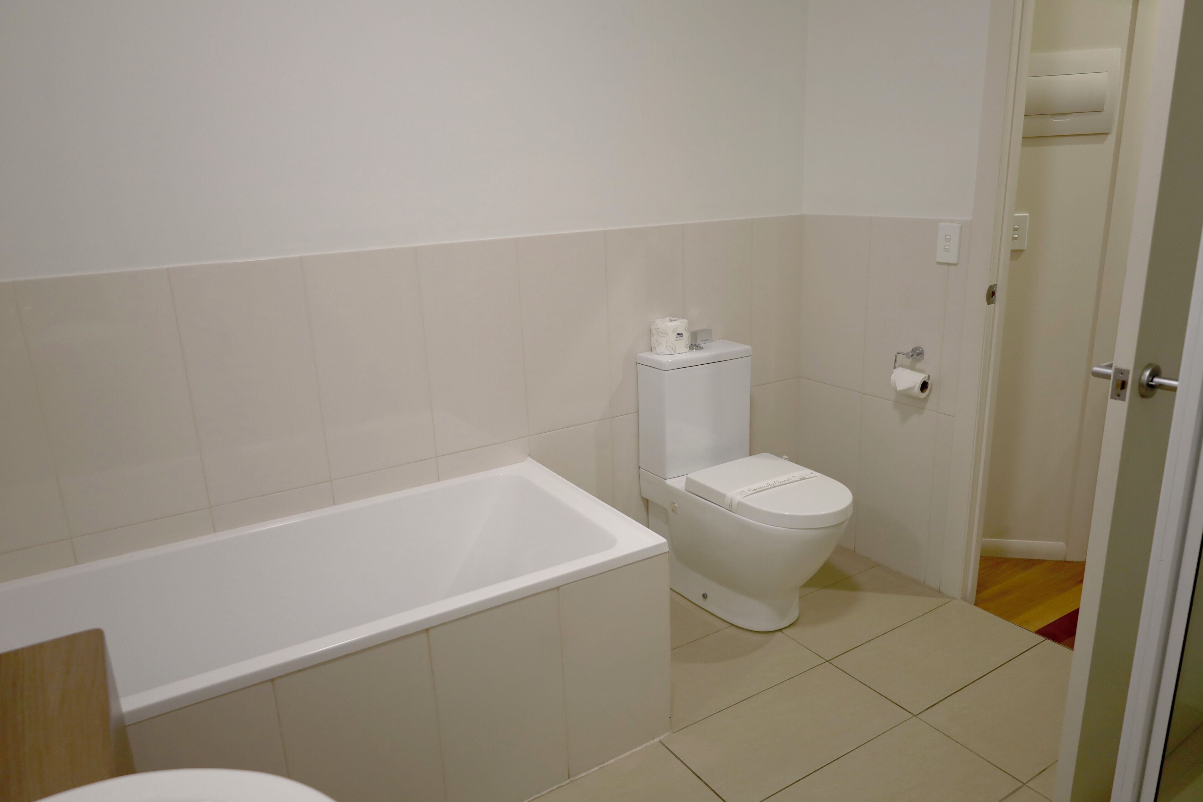 Et badeværelse med et hvidt badekar, toilet og flisebeklædte vægge.