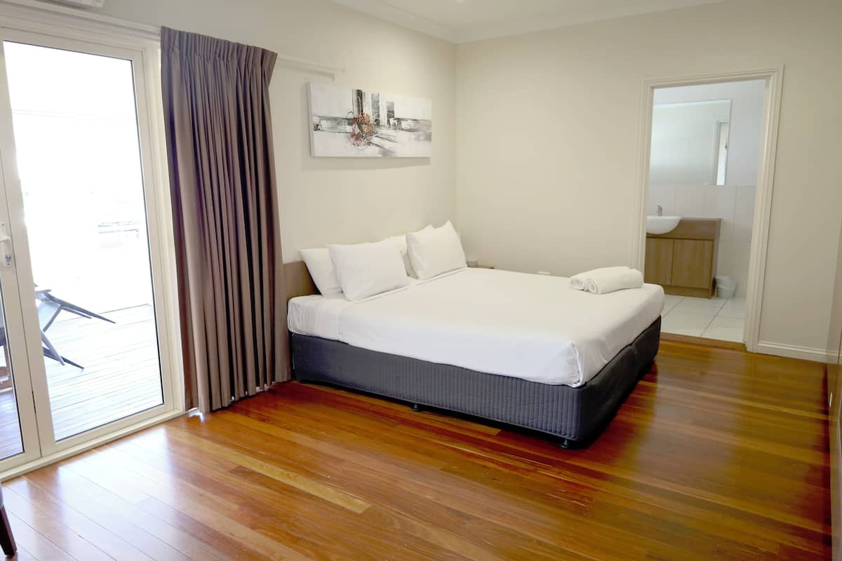 Quarto com cama grande, porta de correr de vidro e banheiro visível através de uma porta adjacente.
