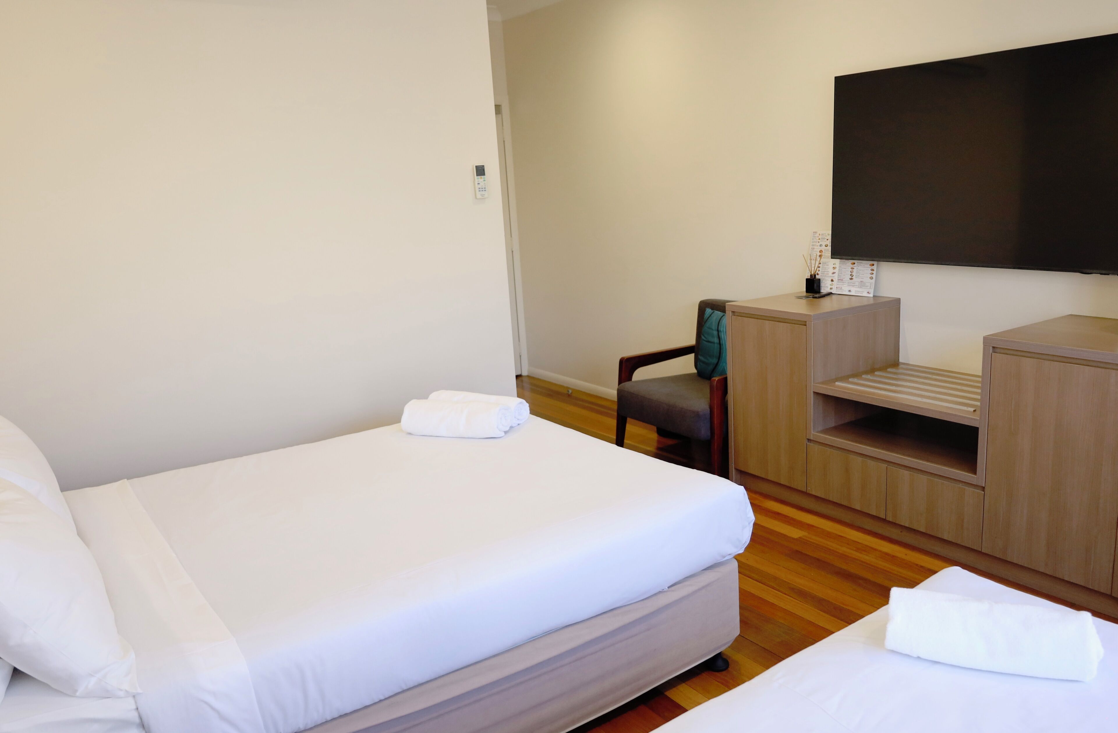 Habitación de hotel con cama, escritorio, silla, televisor y un pequeño estante con control remoto.
