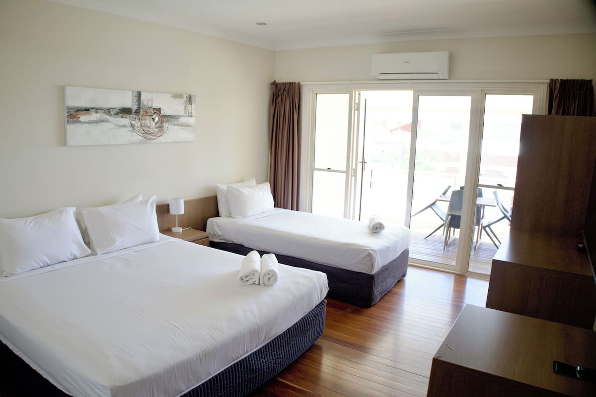 Quarto de hotel com duas camas, uma janela grande e uma porta deslizante para área externa.