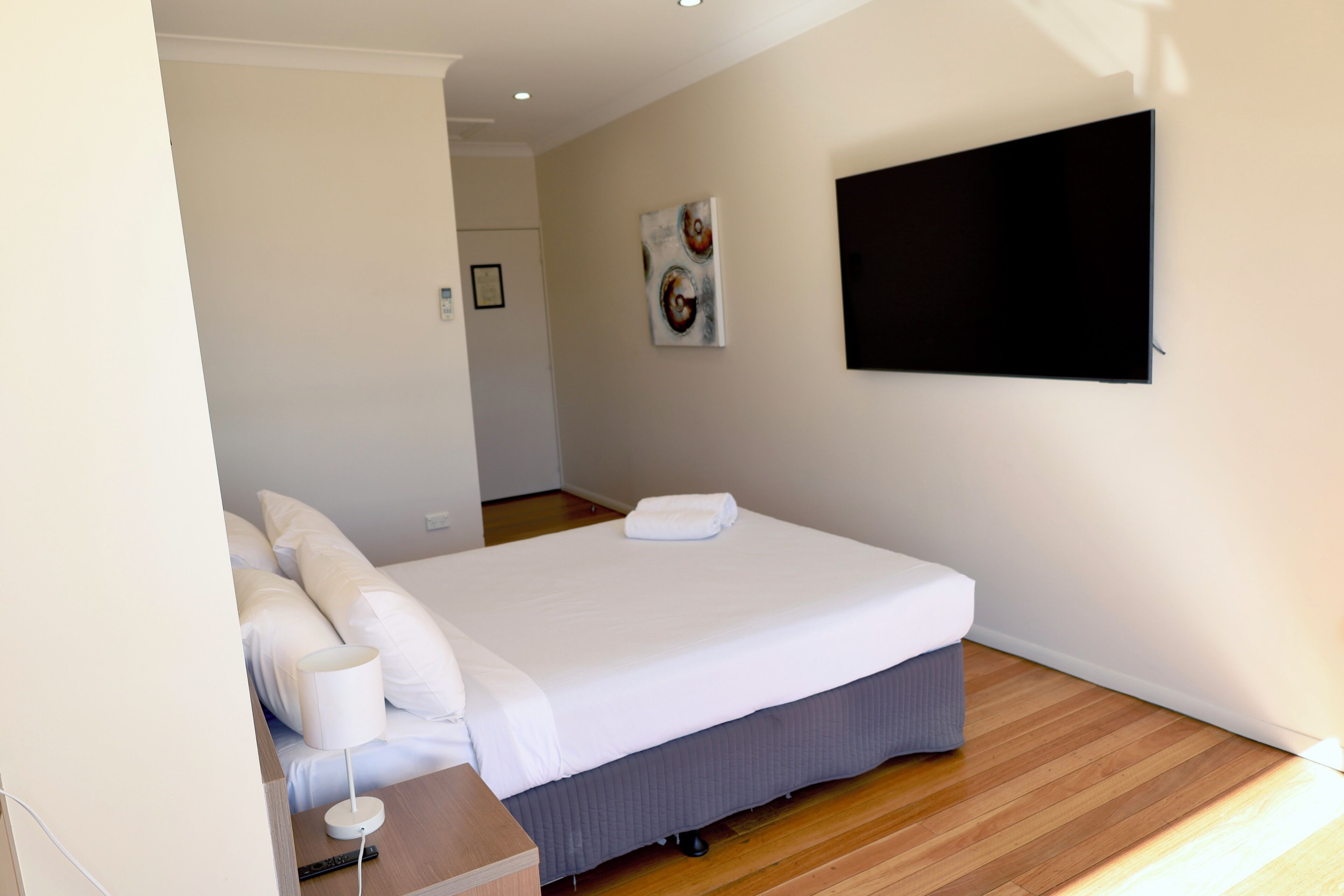 A hotel room with a large bed, a flat-screen TV mounted on the wall, and a wooden floor.