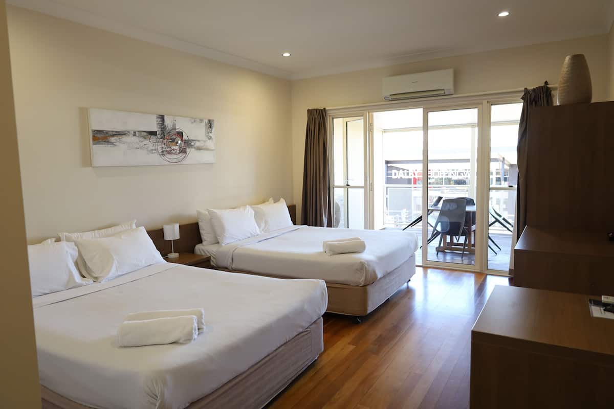 Quarto de hotel com duas camas, uma janela grande, um quadro na parede e uma escrivaninha com abajur.