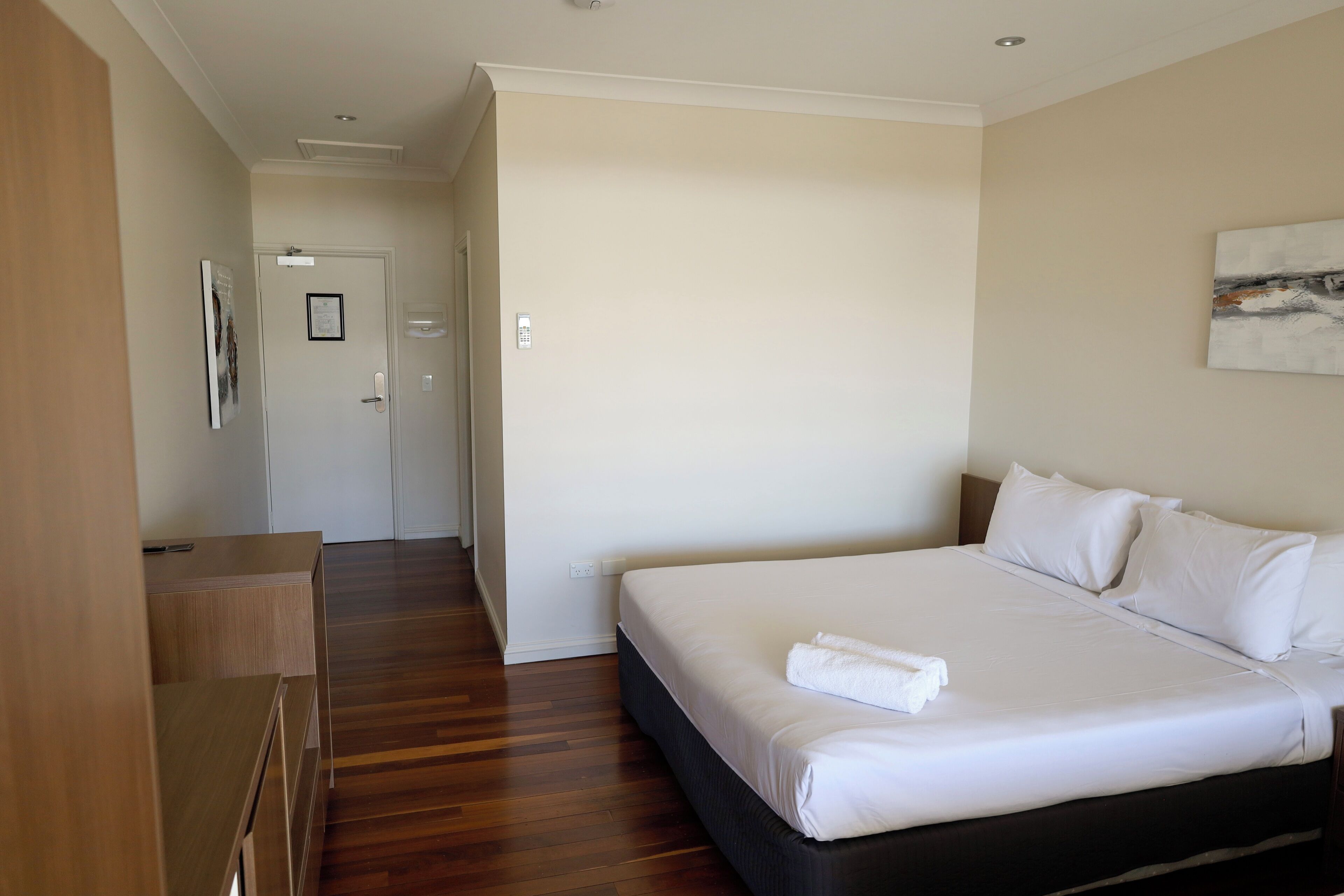 A hotel room with a large bed, wooden flooring, a desk, and a door leading to another room.