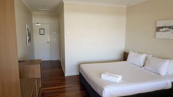 A hotel room with a large bed, wooden flooring, a desk, and a door leading to another room.