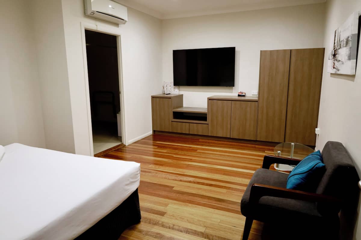 Quarto de hotel com cama, sofá, televisão, pequena cozinha e guarda-roupa.