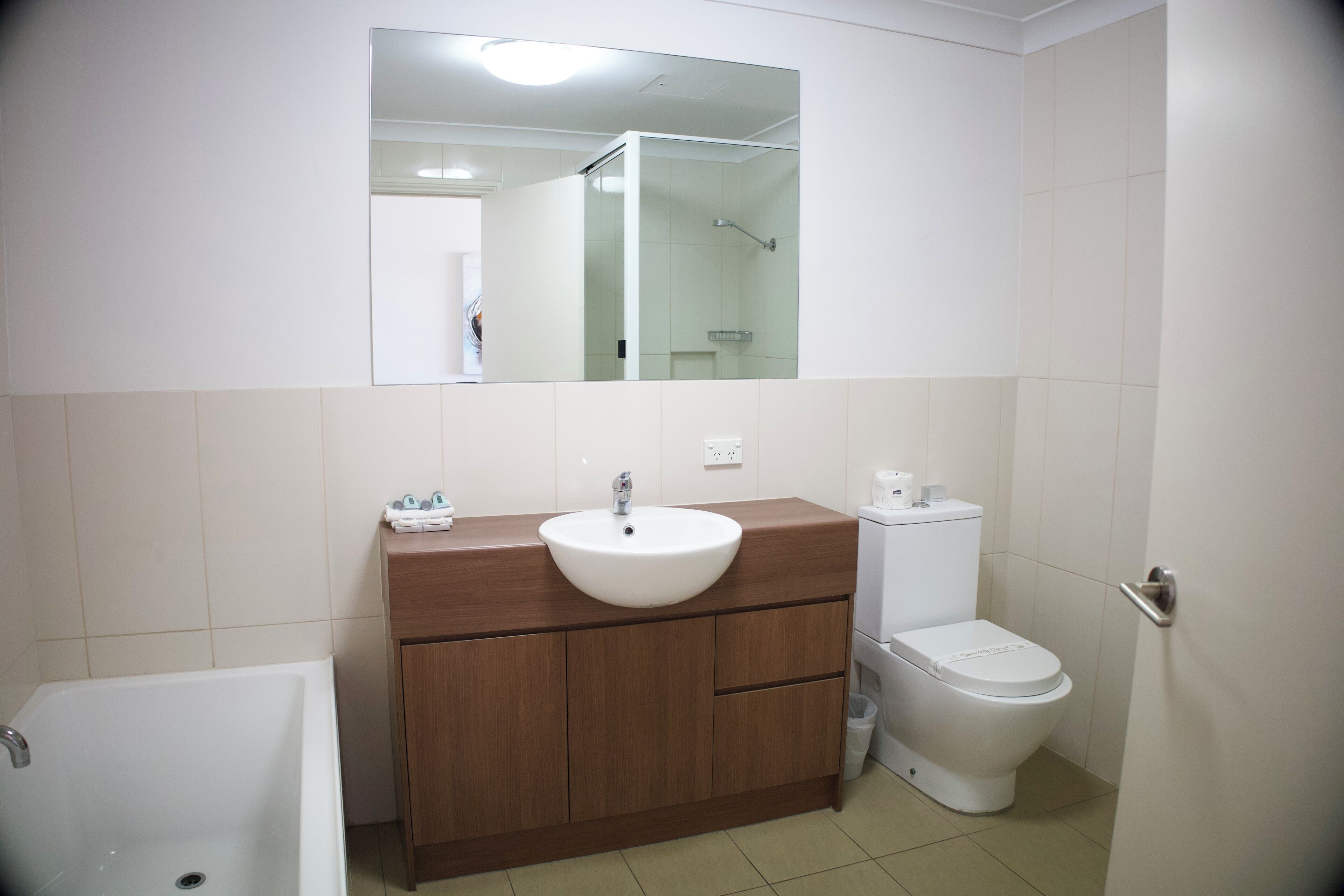 Ein Badezimmer mit weißem Waschbecken, Holzkommode, Spiegel, Toilette und Duschbereich.