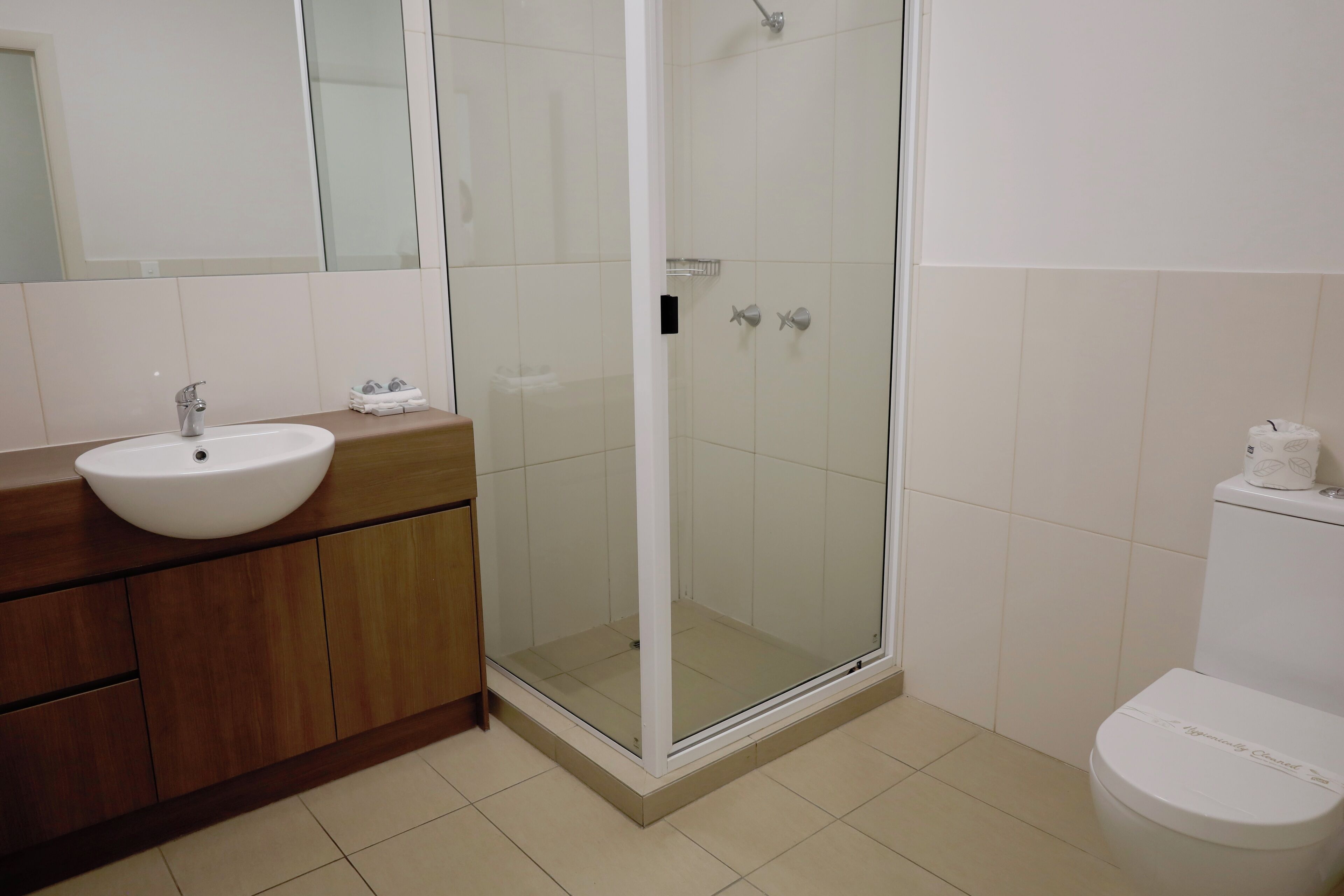 A bathroom with a white sink, wooden vanity, glass shower enclosure, and a white toilet.