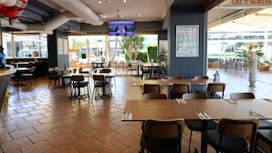 Ein Restaurant mit Fliesenboden, Holztischen und -stühlen, Deckenventilatoren und einem großen Fernsehbildschirm.