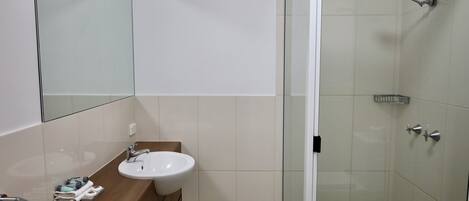 A bathroom with a sink, mirror, and shower.