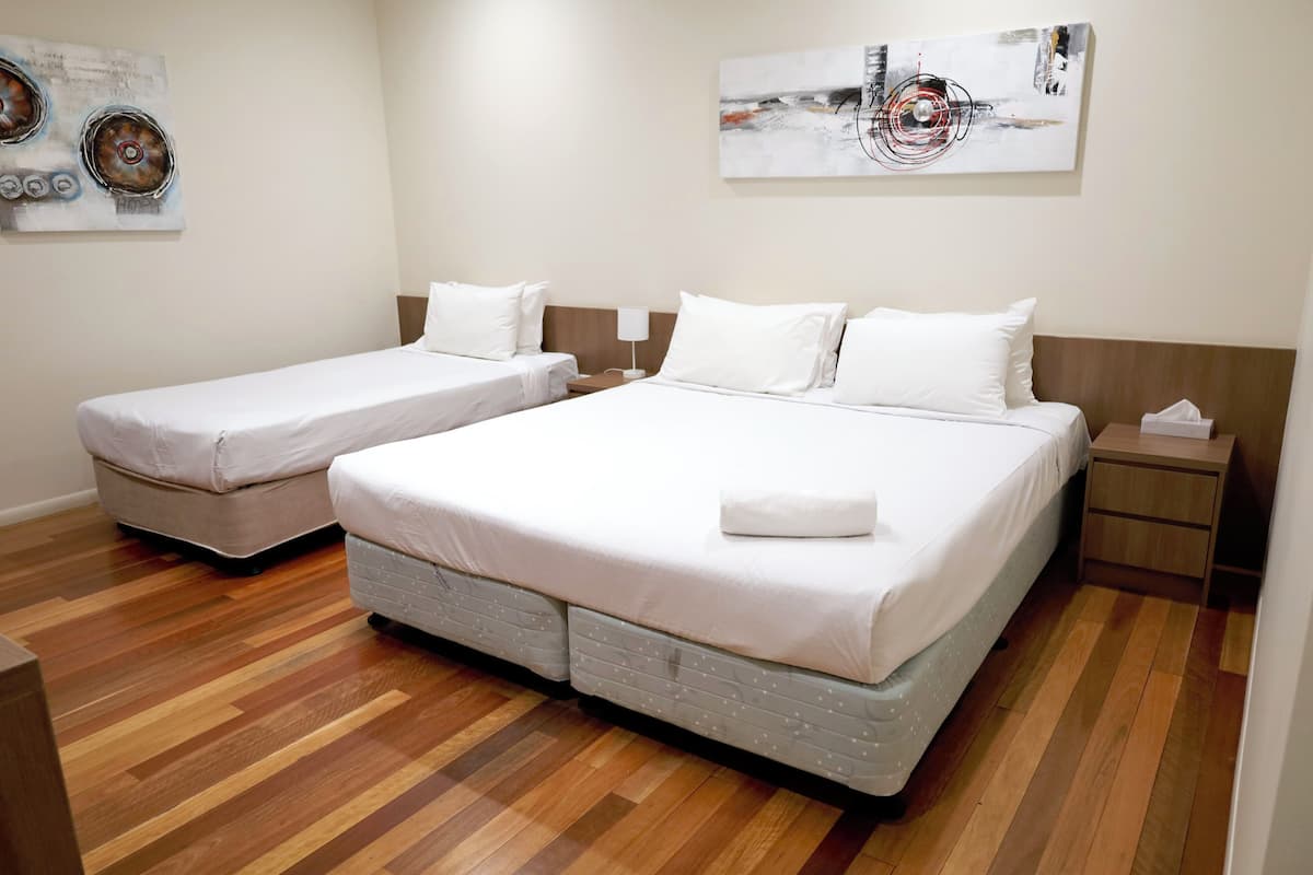 Quarto de hotel com duas camas de solteiro, uma cama grande, piso de madeira e obras de arte nas paredes.