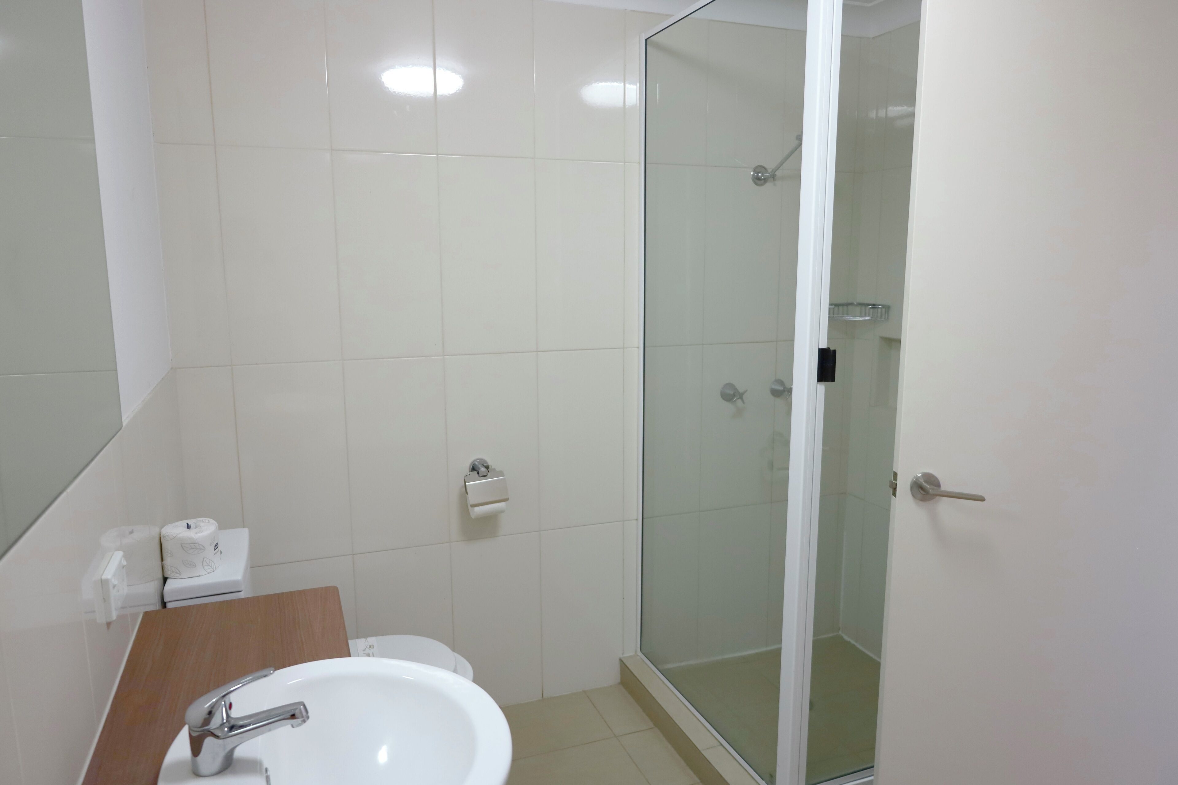 Ein Badezimmer mit weißem Waschbecken, einem Spiegel, einer Toilette und einer Duschkabine.