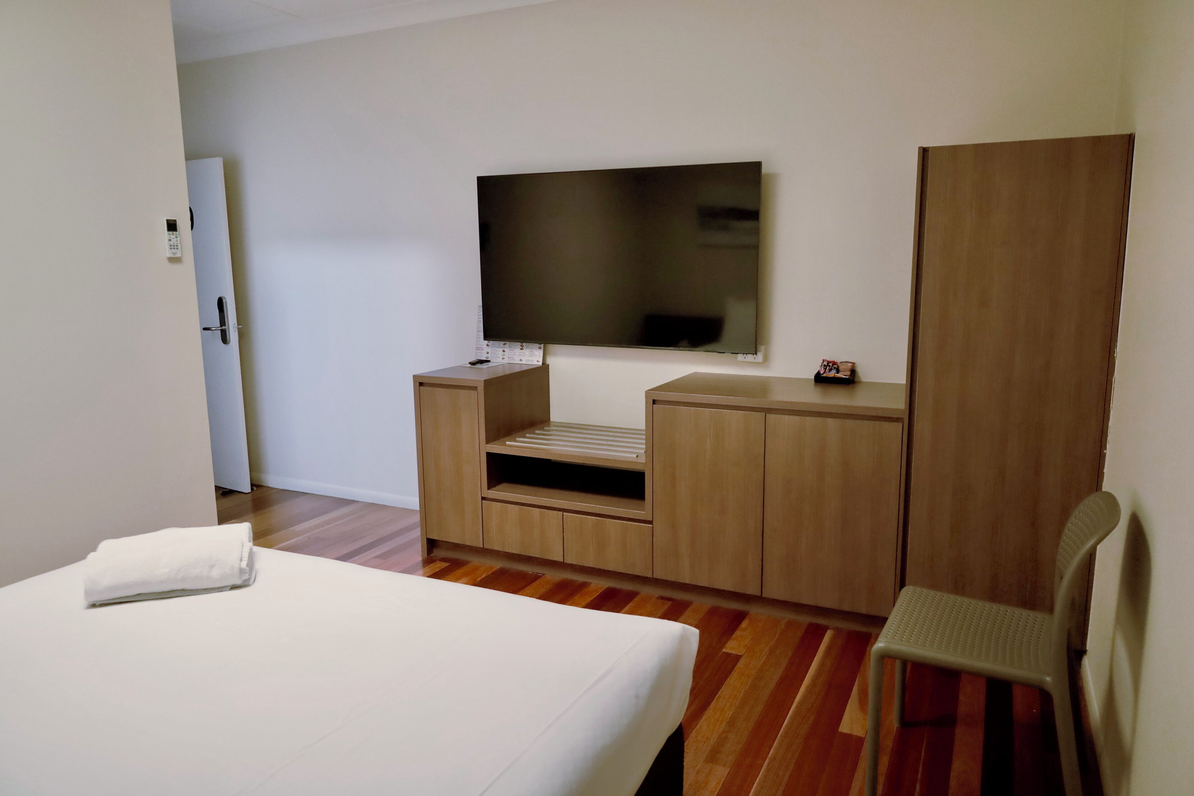A hotel room with a bed, a TV mounted on the wall, a wooden wardrobe, and a chair.