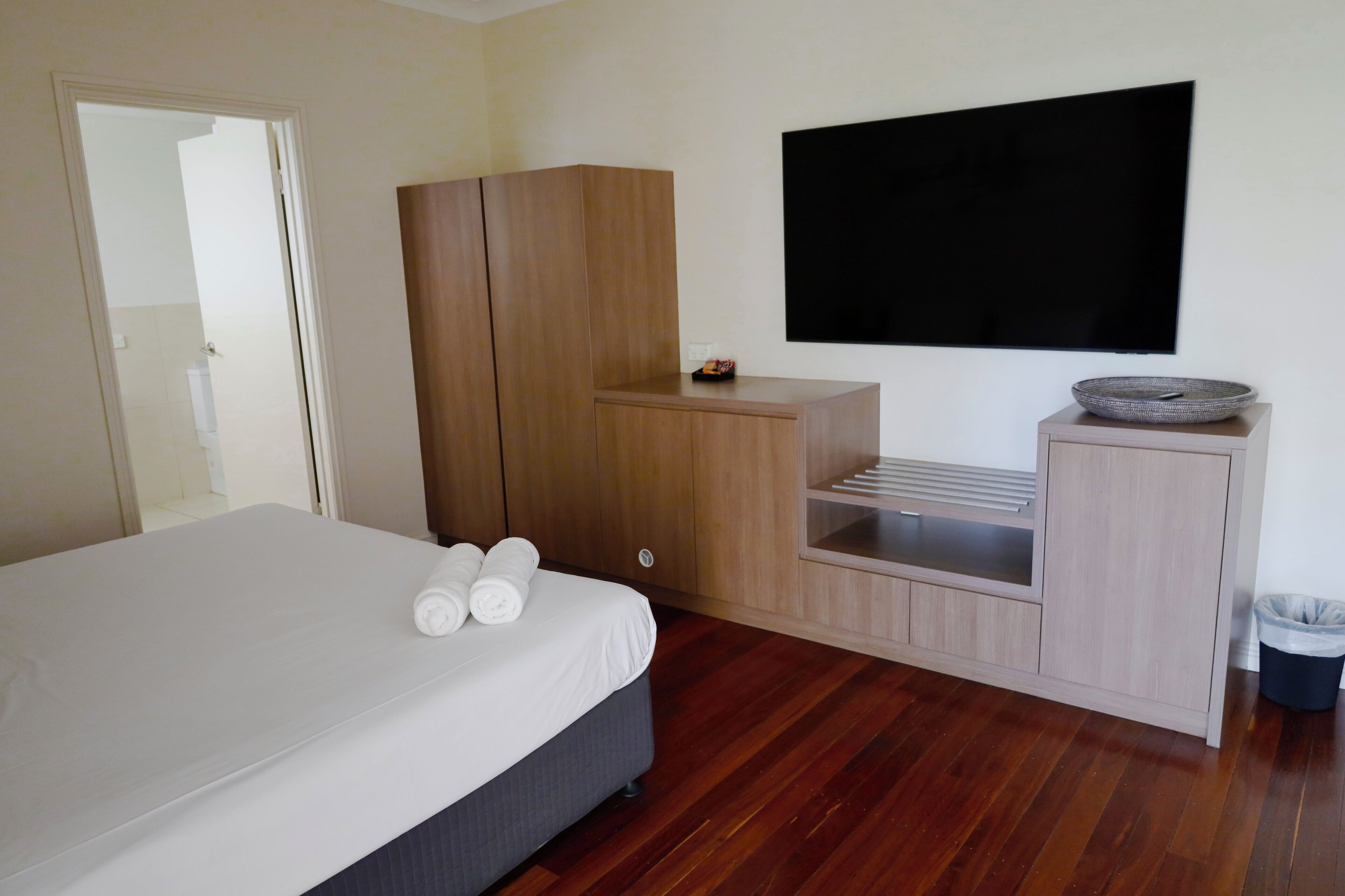 A bedroom with a bed, wooden wardrobe, TV, and a small table with a bowl.