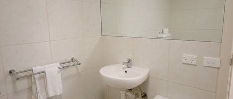 Un baño con lavabo, espejo, toallero y una pequeña mesa con artículos de aseo.