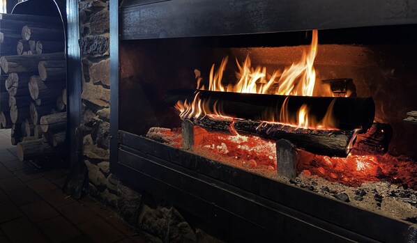 A fireplace with burning logs and flames, set in a stone wall interior. - Great Lake Hotel (Miena)