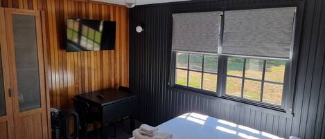 A room with a bed, a desk, a television, and a window with blinds.