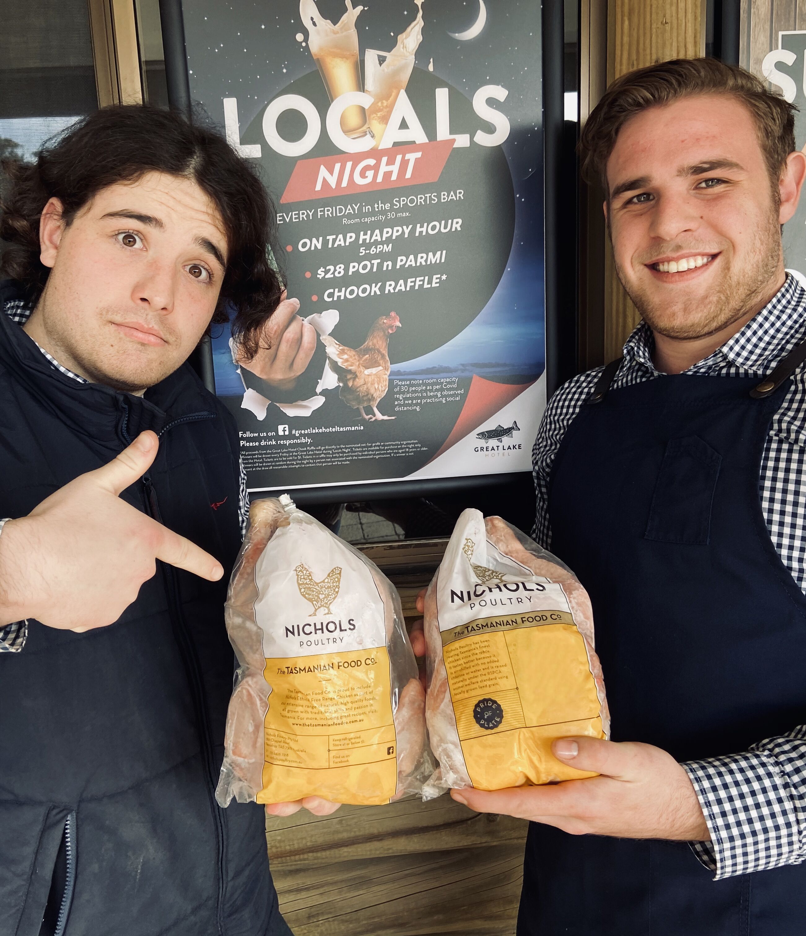 Two individuals holding bags of poultry products in front of a sign advertising a 'Locals Night' event at a hotel.