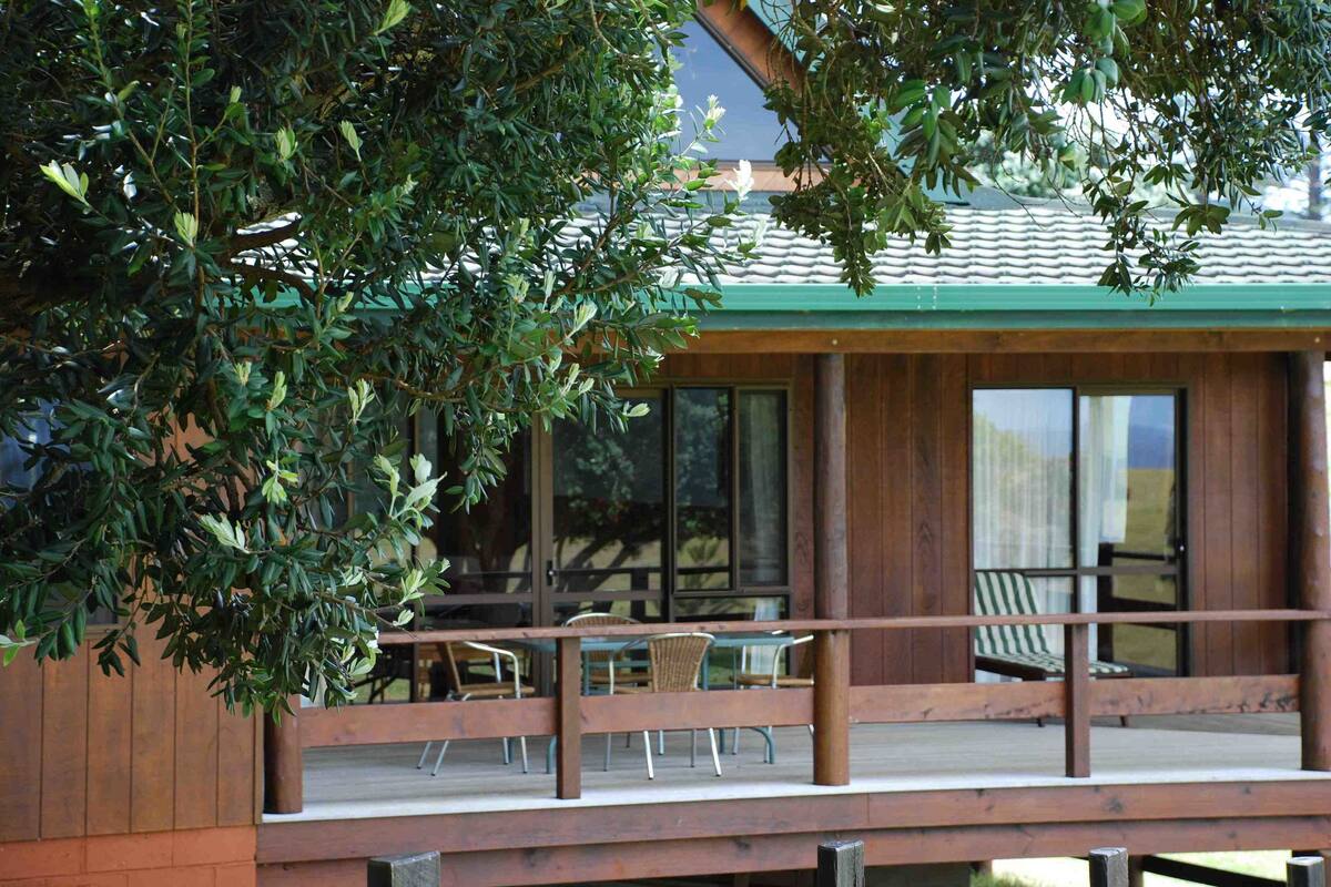 Um deck de madeira com área de estar ao ar livre, grandes janelas e vista para um edifício com telhado verde.