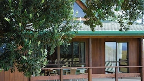 Une terrasse en bois avec des sièges d’extérieur, de grandes fenêtres et une vue sur un bâtiment doté d’un toit végétalisé.