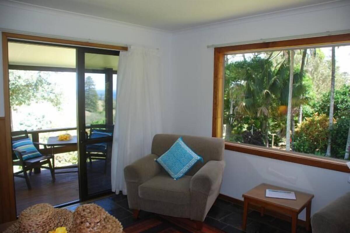 Quarto com porta de vidro deslizante para um deck exterior, uma poltrona bege com almofada azul e uma pequena mesa de madeira.