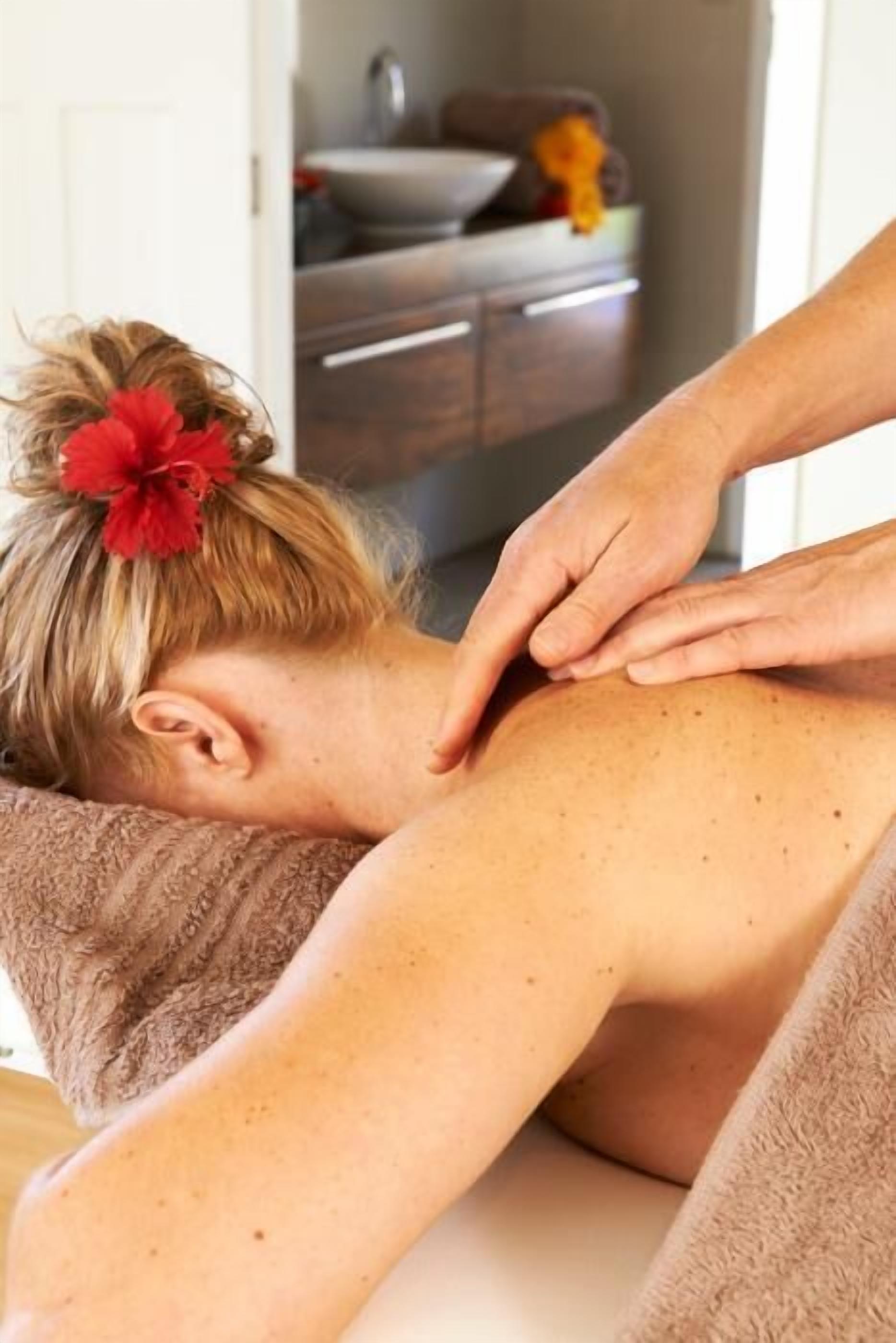 Iemand ontvangt een massage in een ruimte met een zichtbare wastafel en kasten op de achtergrond.