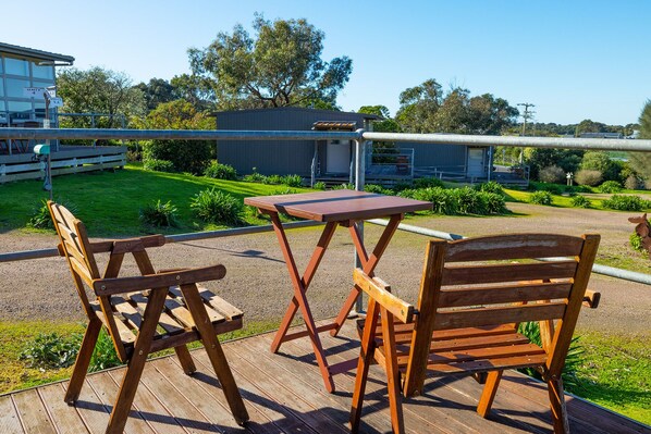 Un área de estar al aire libre con sillas y una mesa de madera, con vistas a un jardín cuidado y un edificio al fondo.