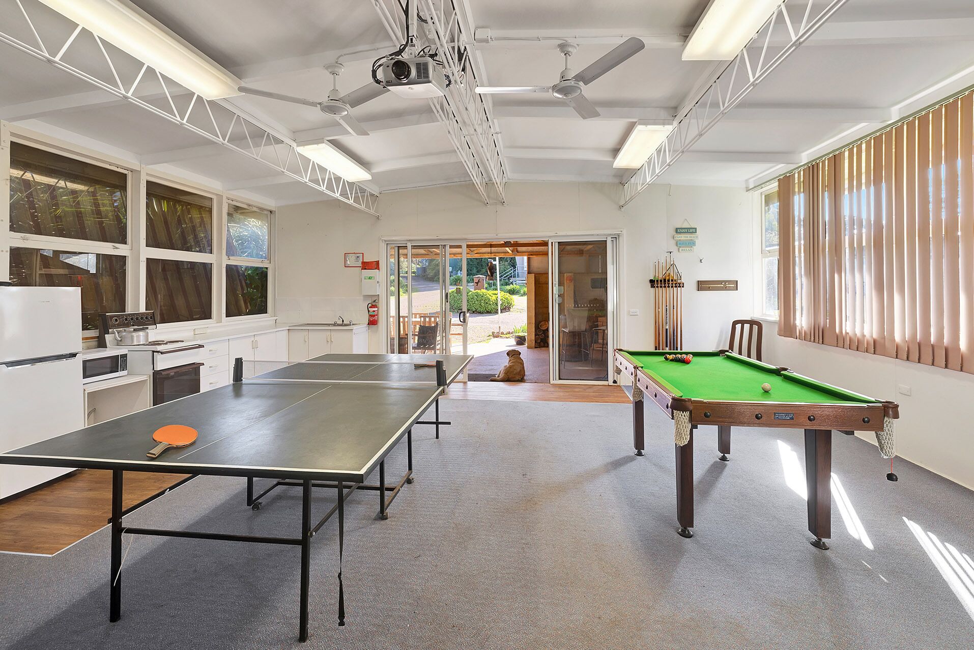 A room with a pool table, ping pong table, ceiling fans, and a kitchenette.