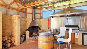 An outdoor cooking area with a wood-fired oven, a charcoal grill, and a seating area with a chair and table.