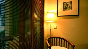Una esquina de una habitación con una silla de madera, una lámpara de pared y un cuadro enmarcado.