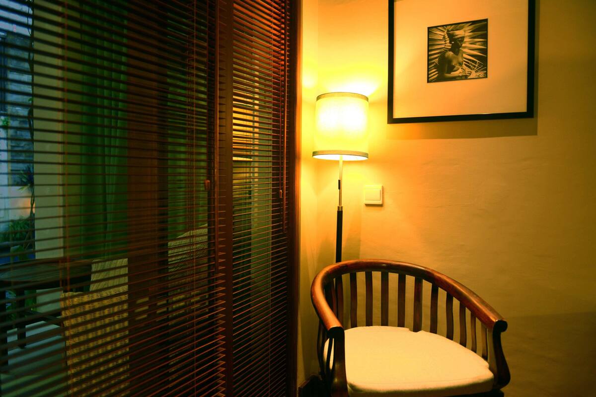 A corner of a room with a wooden chair, a wall-mounted lamp, and a framed picture.