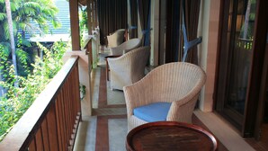 Un balcón con mobiliario de mimbre, una mesa de madera y vistas a la vegetación.