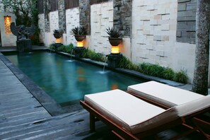 A serene outdoor pool area with a wooden deck, lounge chairs, and decorative planters along the water's edge. - Cinta Grill & Inn (Ubud)