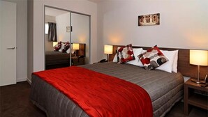 A hotel room with a large bed, a mirror, two bedside tables with lamps, and a wall-mounted artwork. - Lincoln Motel (Lincoln)