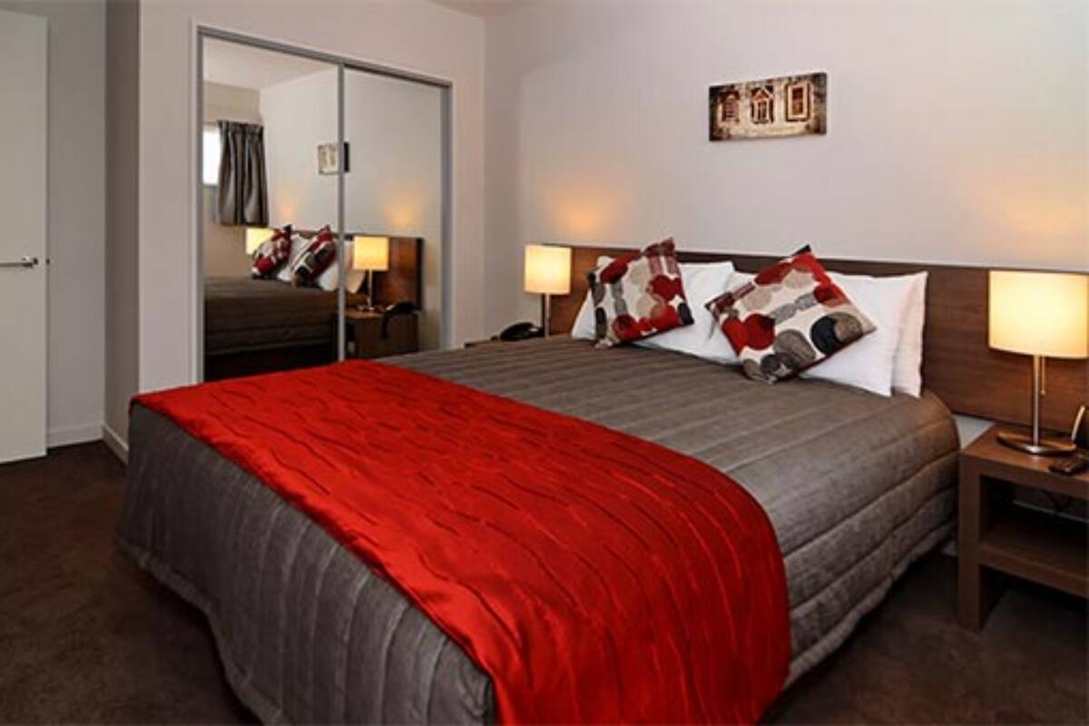 Una habitació d'hotel amb un llit gran, un mirall, dues taules de nit amb làmpades i una obra d'art penjada a la paret.