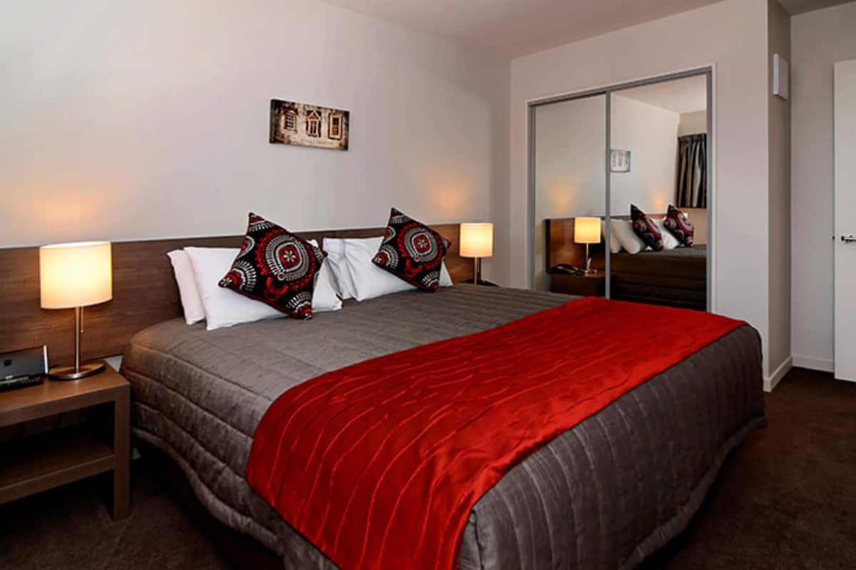Habitació d'hotel amb un llit gran, dues taules de nit, un taulell, un mirall i un armari.