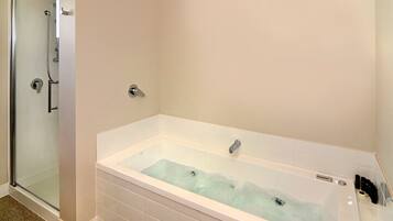 A bathroom with a glass-enclosed shower, a white bathtub, and a white tiled floor.