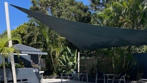 Une piscine dotée d’une terrasse carrelée, entourée de palmiers et agrémentée d’un espace ombragé.